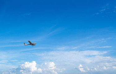 Fototapeta na wymiar Plane flies in the blue sky against the background of clouds