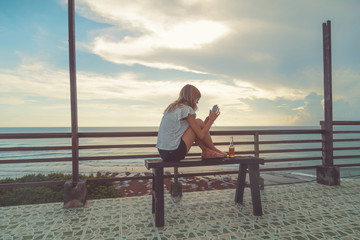 Girl using cellphone on the ocean shore.