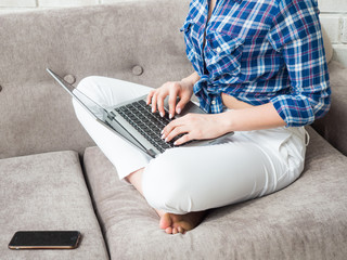 woman is working sitting on the sofa. Hands are holding mobile phone and working with a notebook