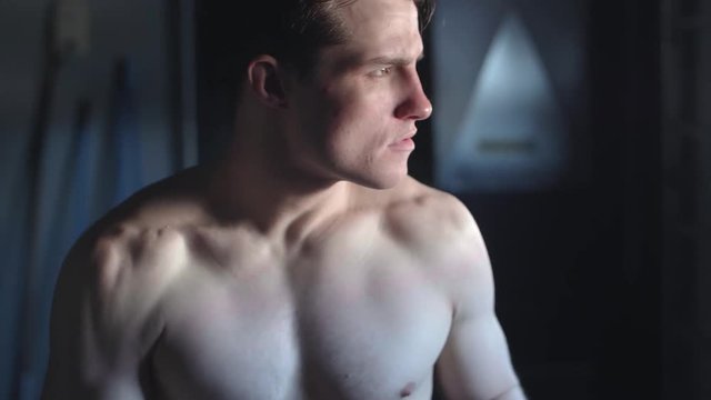 Cinematic shot tilting up across the sexy muscular body of a young MMA fighter who turns to look directly at the camera with a serious mean face SLOW MOTION
