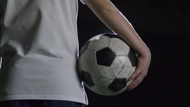 Closeup rear view of boy holding soccer ball while standing against lightning projector in dark arena