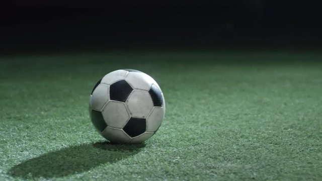 Tracking shot of soccer ball on playing field with artificial turf in low key lightning