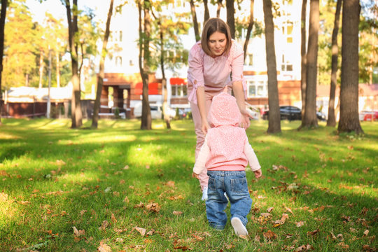 Mother with adorable little girl playing together in autumn park