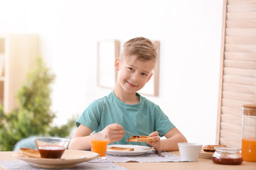 Cute little boy spreading jam onto tasty toasted bread at table