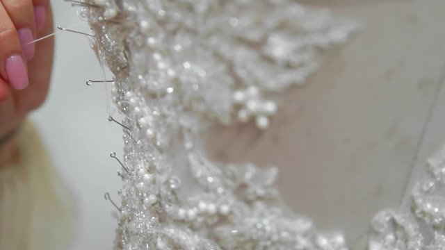 Close-up fashion designer for brides in his Studio pins needles lace wedding dress. Seamstress creates an exclusive wedding dress. Secure with pins and needles outline. Small private business. Sew