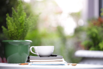 White cup and notebooks with green plant at outdoor