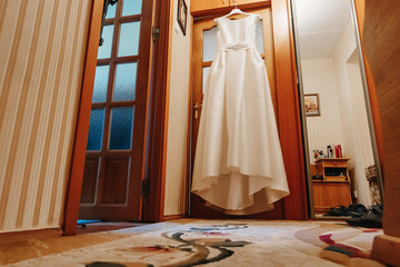 Obraz na płótnie Canvas A wedding dress hanging in a doorway in a room on a brown background. Family, marriage, holiday, celebration, wedding.