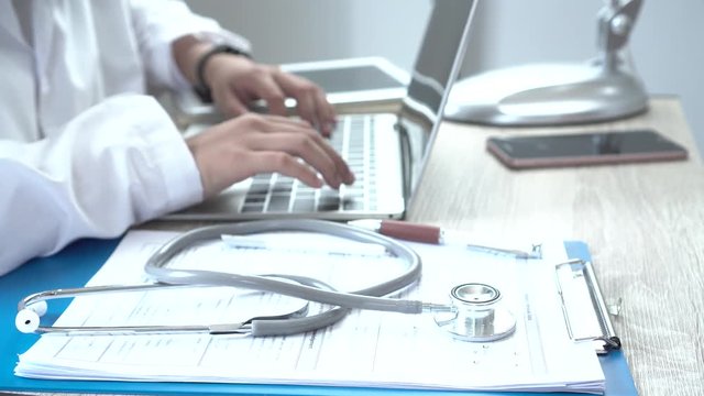 Healthcare and medical concept, Doctor's working searching information about Patient database through internet laptop computer and have Stethoscope on desk hospital office, selective focus