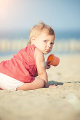 Baby playing on the sandy beach near the sea. Cute little girl in red dress with sand on tropical beach. Ocean coast.