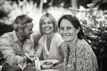 A group of friends gathered to share a meal around a table in the garden. Focus on a beautiful woman looking at the camera