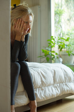 Mature woman sitting on edge of bed with chin in hands