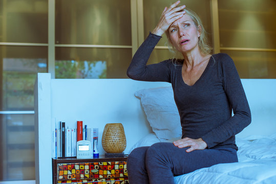 Mature woman sitting on bed with hand on forehead and upset expression on face