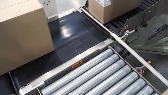 Cardboard boxes on conveyor belt in factory. Clip. Cardboard boxes on conveyor belt in distribution warehouse. Packed courier on production line against grey background