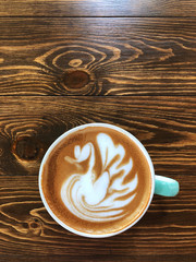 Beautiful Swan shape latte art coffee in white and green cup on wooden table ; love coffee, Top view and copy space.