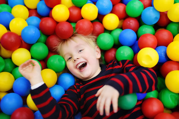 Happy little boy having fun in ball pit with colorful balls - obrazy, fototapety, plakaty