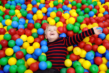 Fototapeta na wymiar Happy little boy having fun in ball pit with colorful balls