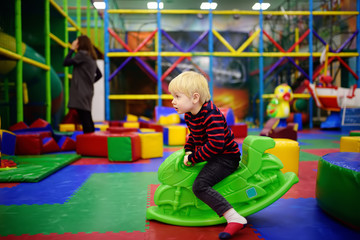 Happy little boy having fun with plastic toy-swing/hopping motorbike in play center