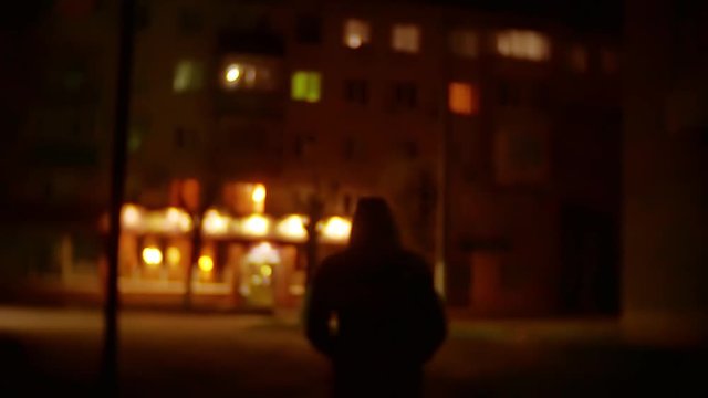 silhouette of man robber in the hood is a night light lantern thief offender. burglar blurred background unknown goes bandit in outdoors the hood plunderer