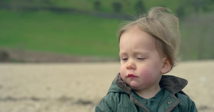 A cute little boy is on the beach on a cold day with the wind blowing in his hair in slow motion 120fps