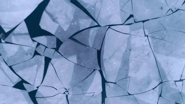 Aerial top view of cracked ice floes. Drone shot flying up over melting ice, global warming, climate change background. Beautiful winter pattern