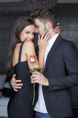 Happy young man with rose holding embrace beautiful woman indoors, love