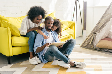 smiling african american parents and little daughter reading book together at home