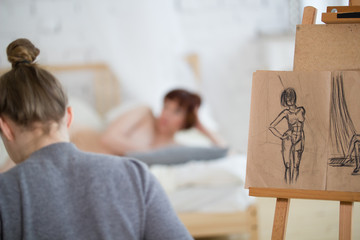 Rear view of female painter draws sketches of nude woman in drawing class
