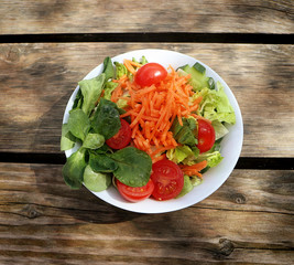 mixed salad, cherry tomatoes, carrots, lettuce,field salad and gherkins on wooden table outdoors