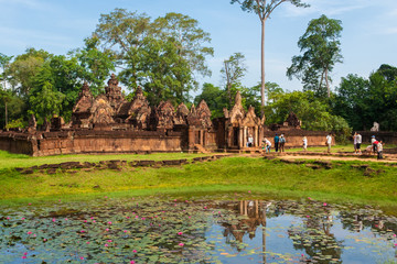 Fototapeta na wymiar Full view of the second enclosure of Cambodia's Banteay Srei (Citadel of the Women) temple and the water lily-filled moat. Tourists walking on the causeway to reach the east gopura entrance. 