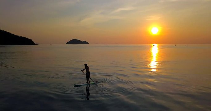 Aerial 4k: Sunset silhouette of a person standing up at paddle board on vacation in Thailand