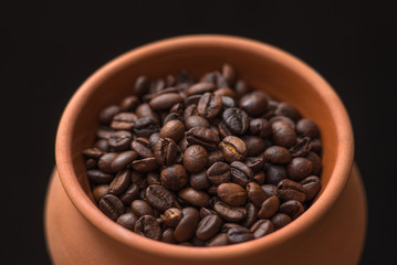 Clay pot filled with coffee beans on black background. Place for text