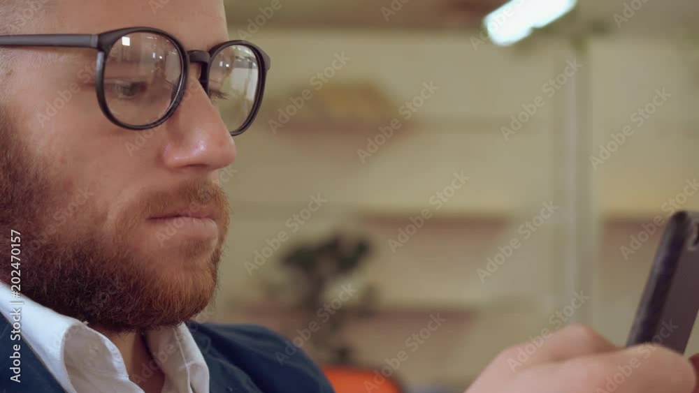 Poster close up redhead handsome man using smartphone. bearded businessman scrolling touch screen on mobile chatting use internet indoors wearing jacket and white shirt