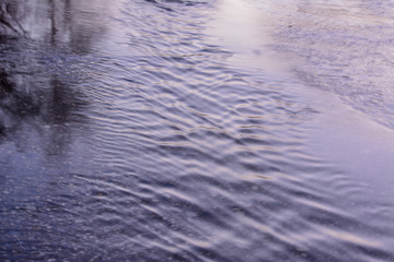 Spring creek flows through the asphalt road. Early spring.