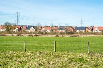Houses of an English village with overhead power cable lines seen from outside field in early Spring - environmental background - 4