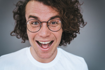 Closeup portrait of excited handsome freckled positive smiling male wears spectacles posing for social advertisement, isolated on grey background with copy space for your promotional information