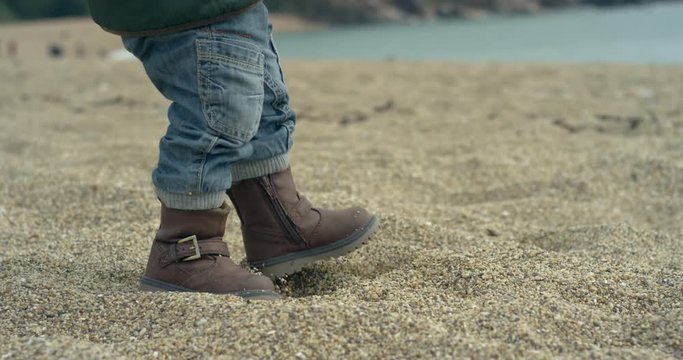 A little boy is walking on the beach in his boots. Slow motion handheld shot.