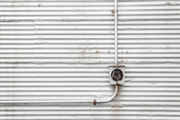 Metal piping on a corrugated metal wall leading to an electrical box with pulled out wires that are taped. 