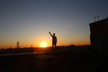 silhouette  man raised  hand up roof  building sunset