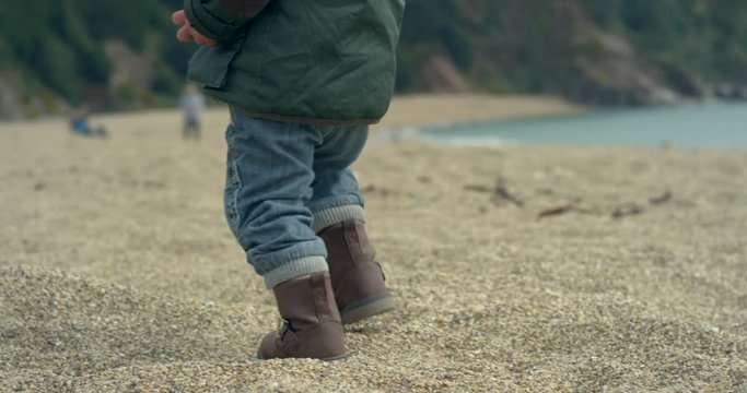 A cute little boy on the beach is walking then falling over