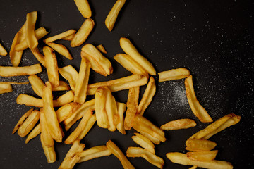 top view of delicious french fries spilled with salt on black