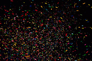 Thousands of confetti fired on air during a festival at night. Image ideal for backgrounds. Multicolor are the confetti in the picture. The sky as background is black. Warm and hot tonality
