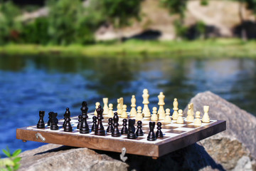 Chess board with chess pieces on rock with river embankment background