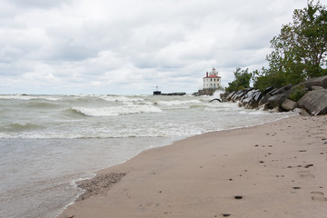 Lighthouse at Mentor Headlands Beach State Park in Ohio with waves crashing on shore and dark clouds overhead. 