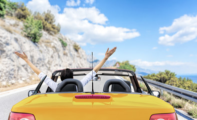 Young woman in a car on the road to the sea against a backdrop of beautiful mountains on a sunny day. - obrazy, fototapety, plakaty