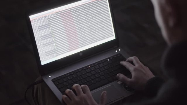 a hacker in a dark room, working behind a laptop, code on the monitor, hacker attacks, web programming and fixing viruses, crashing the site,