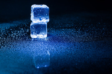 Blue ice cubes reflection on black table.