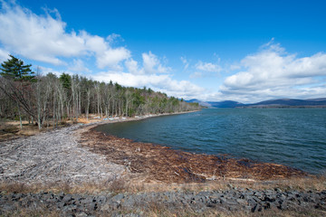 Shoreline and Distant Mountains at the Ashokan Reservoir. Beautiful Spring Morning, Blue Sky with Clouds and Driftwood and Stone Wall along the shore. NYC Water Supply and Tourist Destination.