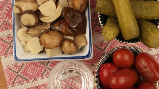 Three salad bowls with pickled cucumber, tomatoes and mushrooms and a glass of the Ukrainian vodka