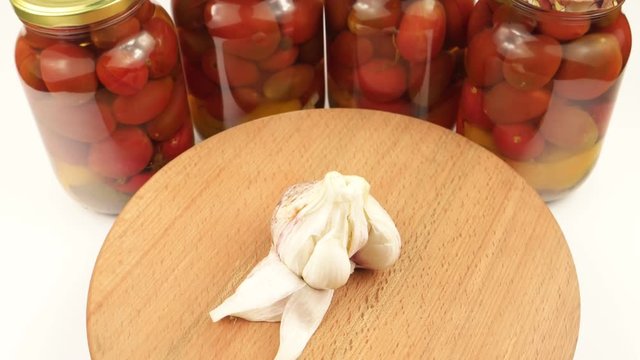The garlic head rotates on a wooden board against the background of glass jars with canned tomatoes