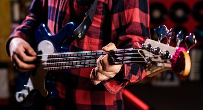 Male hands holds bass guitar, play music in club atmosphere background. Play guitar concept. Fingers clamp strings on bass guitar neck. Closeup of blurry male hands playing the guitar.